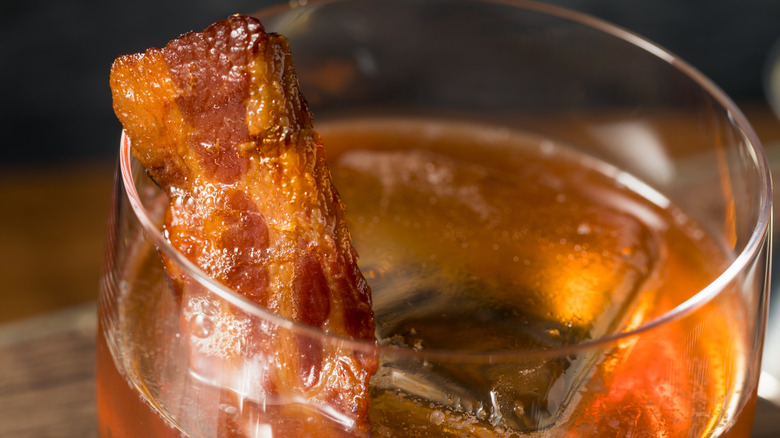 Closeup of a glass of bourbon with a bacon strip garnish
