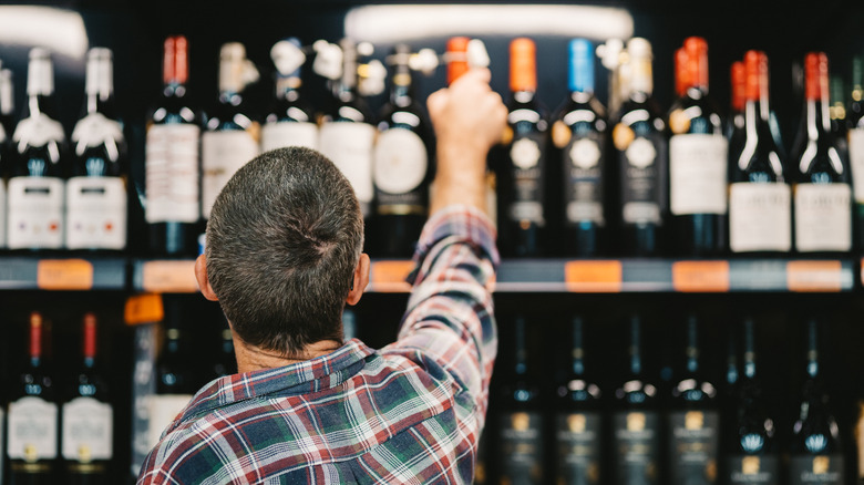 man taking bottle of wine off top shelf 