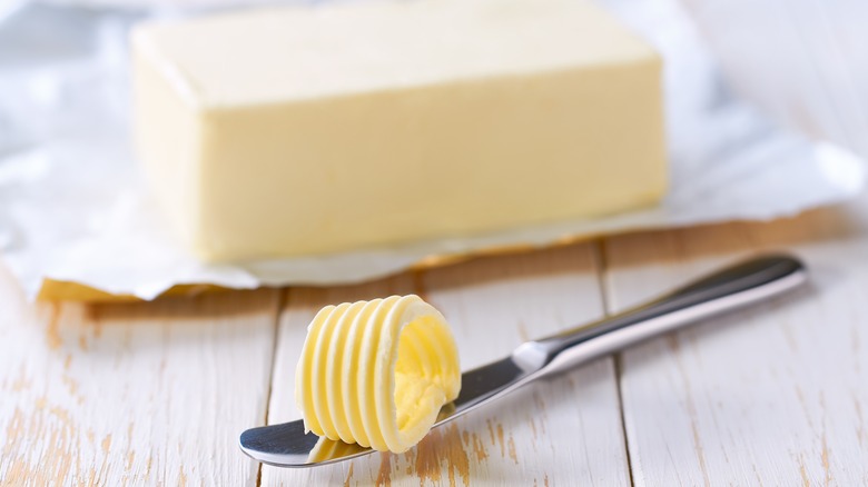 Knife with slice of butter in front of stick of butter