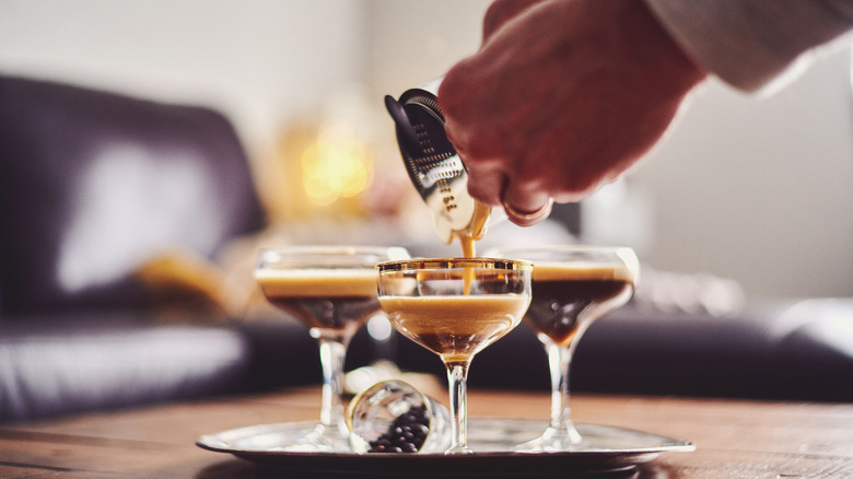 hand pouring espresso martinis into glasses