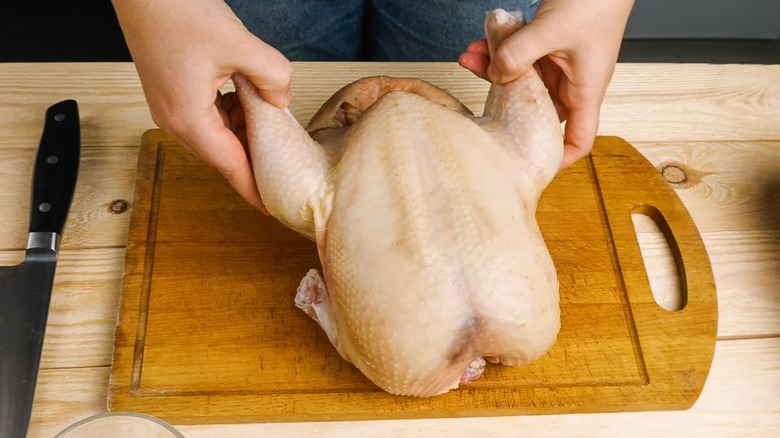 holding whole raw chicken on board