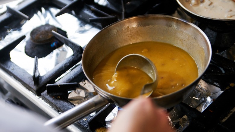 Hand mixing gravy in a pot on a stovetop