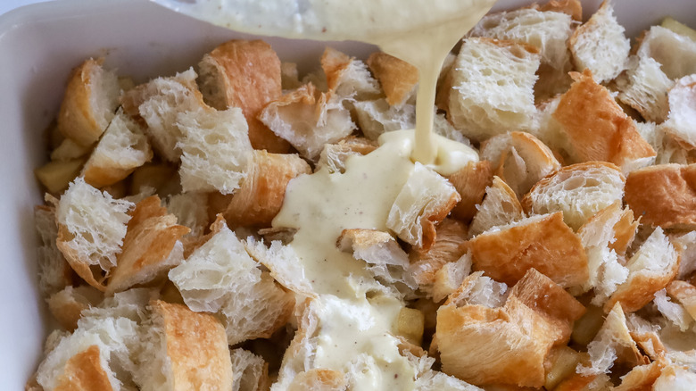 Liquid being drizzled over croissants in a baking pan