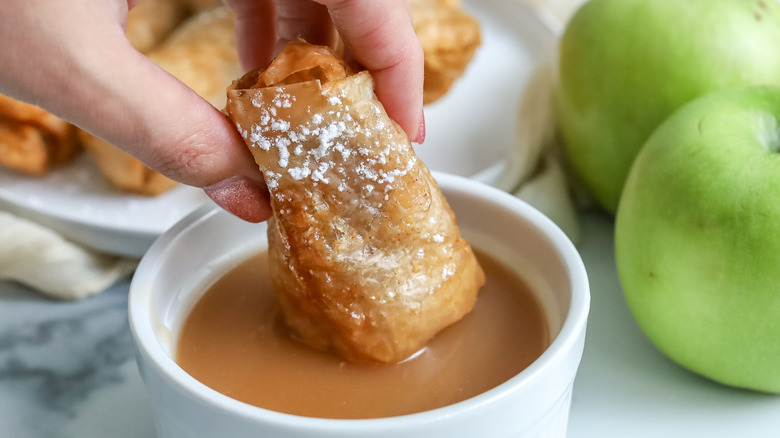 apple pie phyllo roll being dipped in caramel sauce