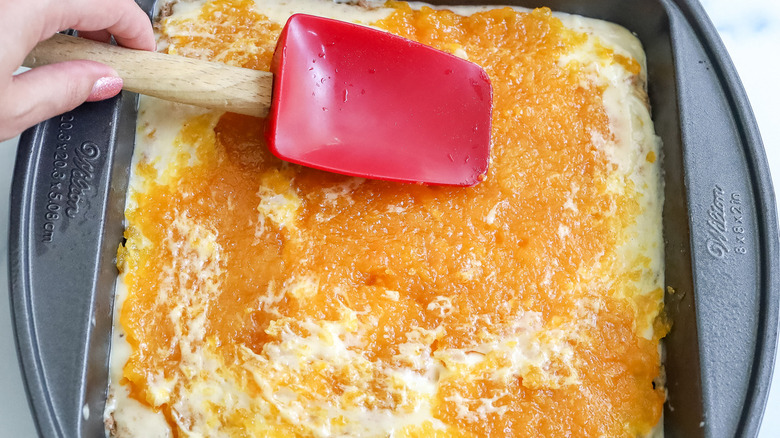 hand spreading apricots on cake