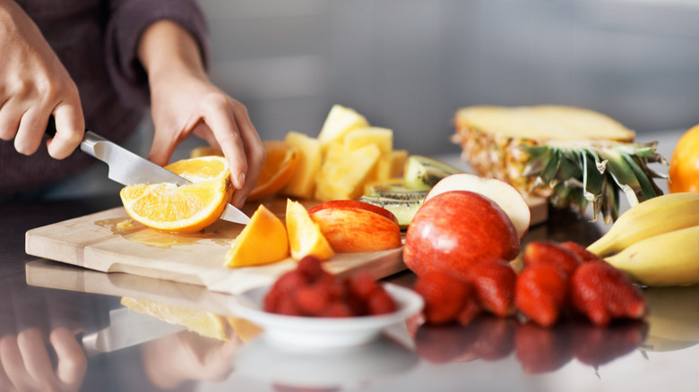 Someone chopping various fruits on a cutting board.