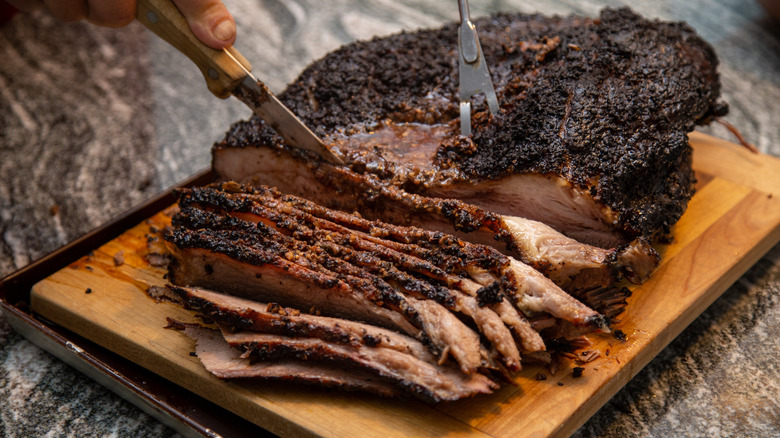 Beef brisket being carved into slices on a wooden cutting board