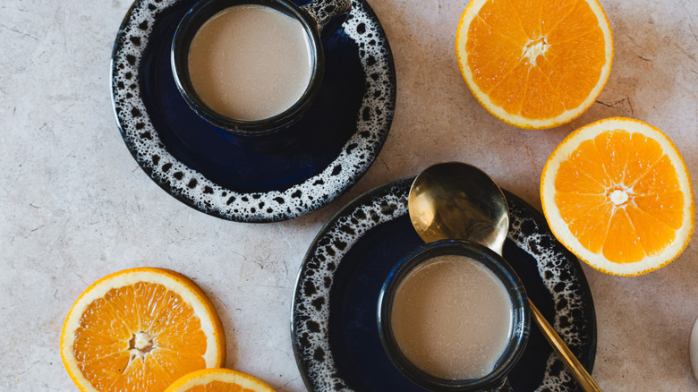 Two cups of coffee with creamer and oranges