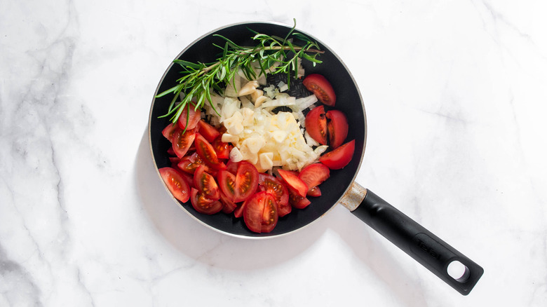 raw tomatoes onion and rosemary in a pan