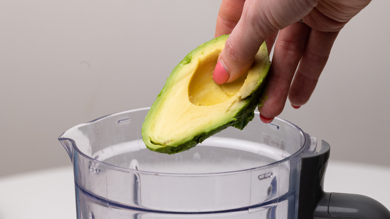 hand placing avocado in blender