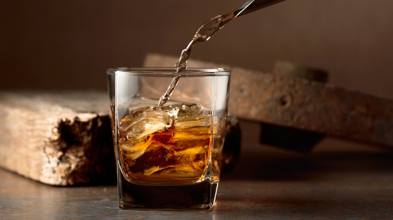 Whiskey being poured into a glass with ice