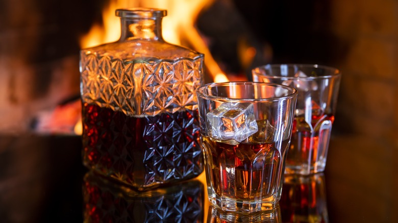 A decanter and two glasses of whiskey near a fire