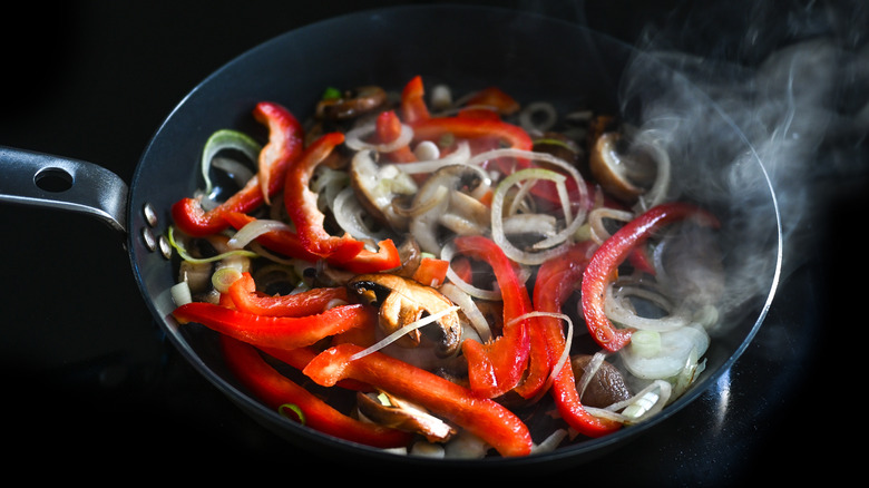 A frying pan cooking red bell peppers, mushrooms and onions