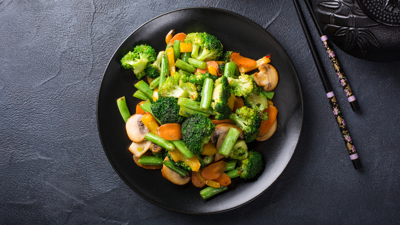 Top-down view of stir fried vegetables on a black plate over a black background