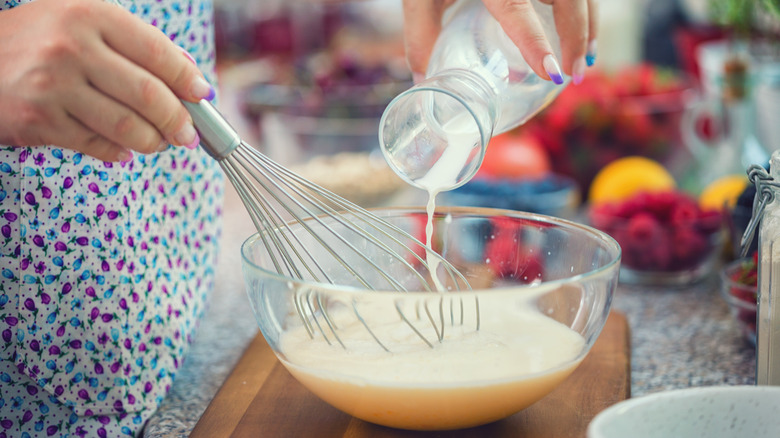 woman adding milk to bowl and whisking