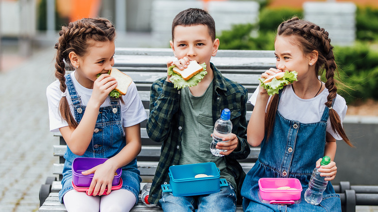 three school children eating sandwiches