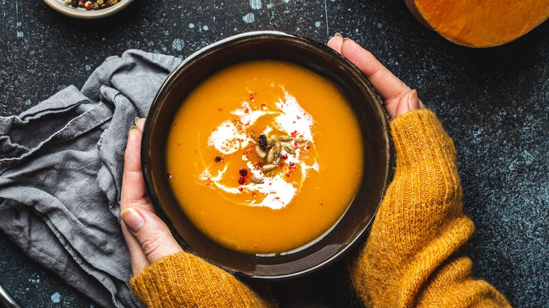 hands enclosing a bowl of pumpkin soup