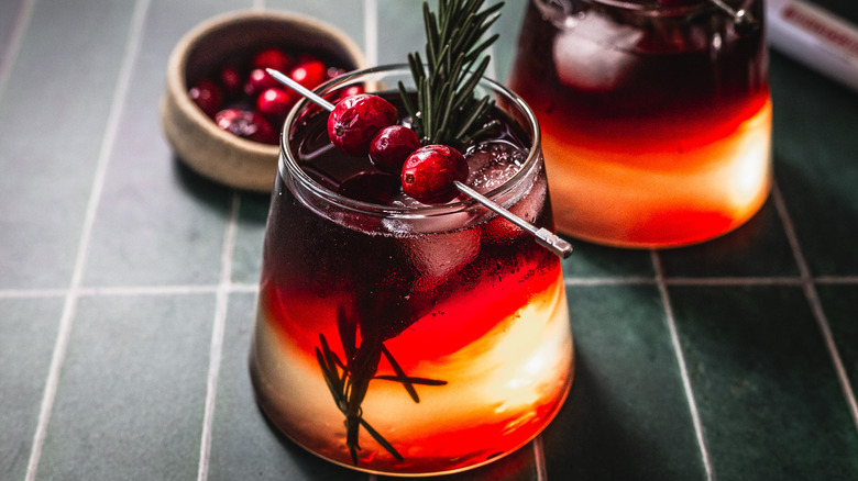 A cocktail with cranberries and a rosemary sprig