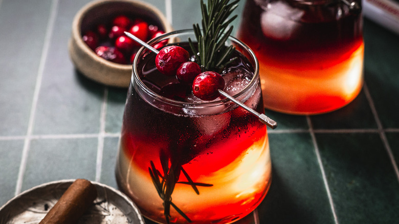 A cocktail with cranberries and a rosemary sprig