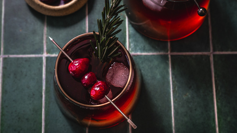 Overhead view of a cocktail with cranberries and a rosemary sprig