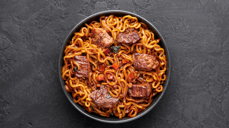 gochujang noodles with cubes of beef in a dark bowl