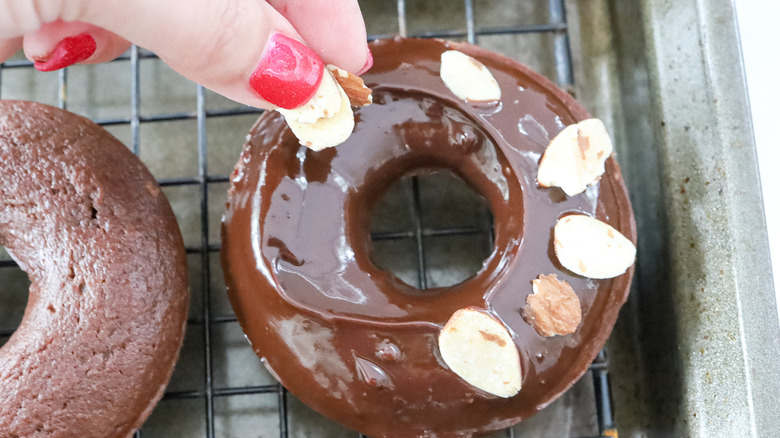 hand placing almond onto donut