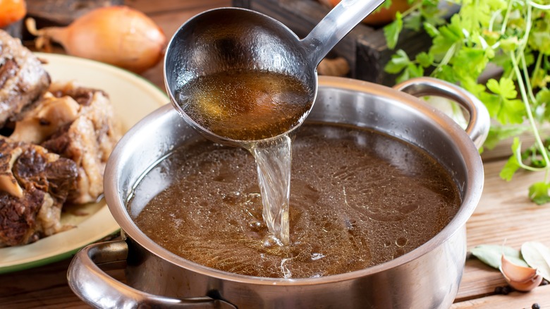 Ladle pouring beef broth into pot