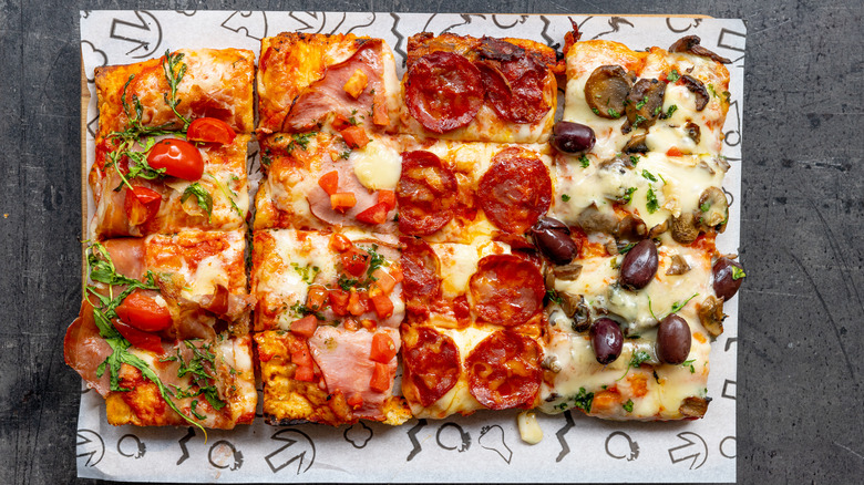 rectangular pizza with various different toppings over a butcher-paper covered tablet