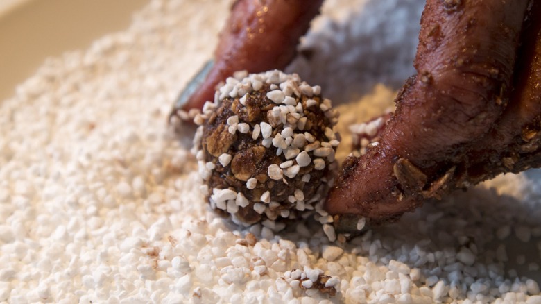 Fingers rolling a ball of cookie dough in Swedish pearl sugar