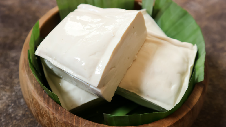 blocks of soft tofu in a wooden bowl with banana leaves 