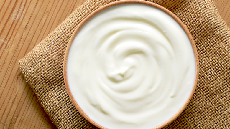 A bowl of plain yogurt on a jute towel on a wooden table