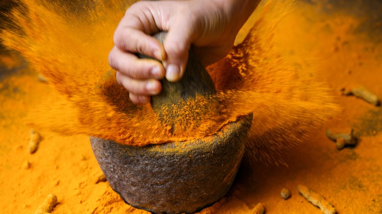 Woman pounding bowl of turmeric