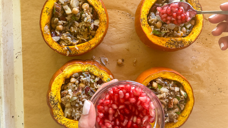 hand adding pomegranates to pumpkins