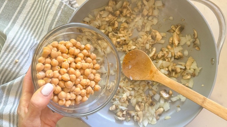 hand adding chickpeas to pan