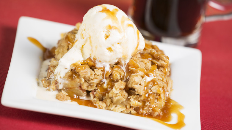 apple betty on a white plate topped with a scoop of ice cream and caramel sauce