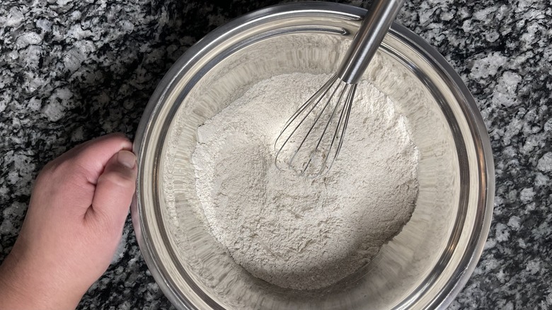 hand with bowl of flour and whisk