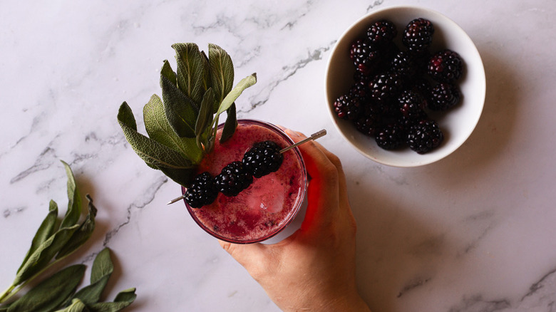 hand serving drink with sage and blackberries