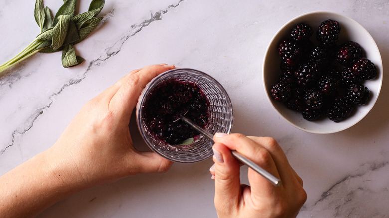 hand muddling berries in glass