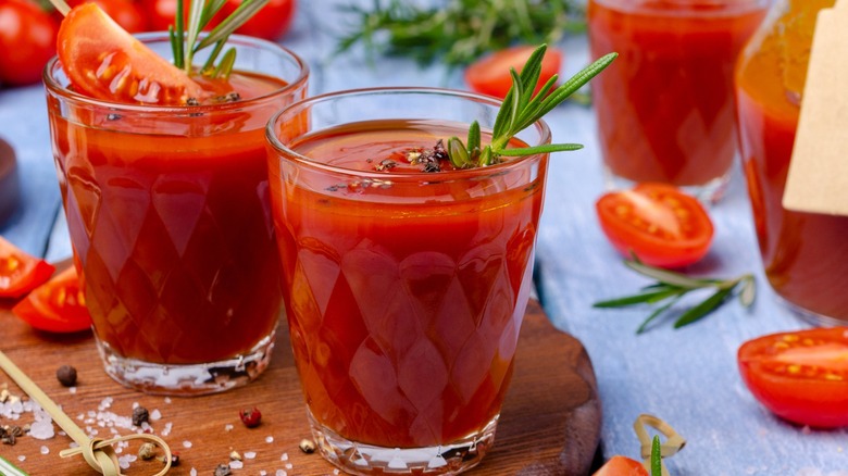 Bloody Mary mix in glasses with raw ingredients on a wooden surface
