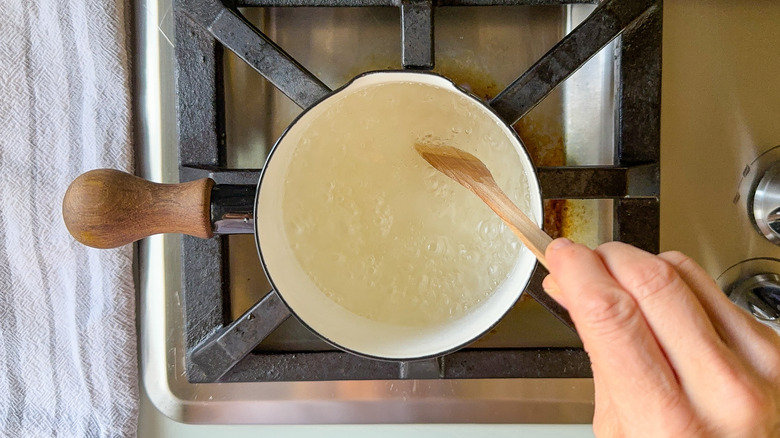 Almond simple syrup boiling in saucepan with wooden spoon