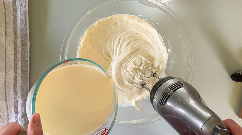 Adding heavy cream to whipped mascarpone in glass bowl