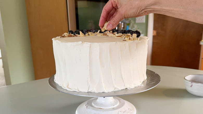 Garnishing blueberry and almond Chantilly cake with fresh blueberries and sliced almonds on cake stand