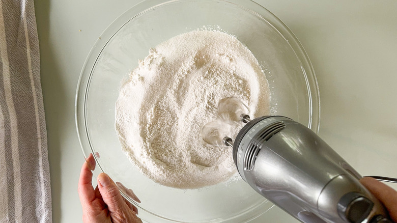 Using hand mixer to combine dry ingredients for cake in glass bowl