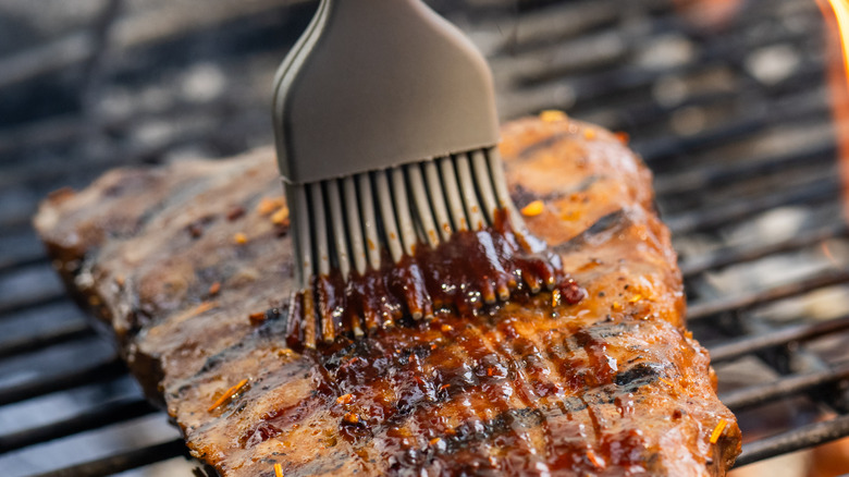 Silicone pastry brush applying glaze to meat on grill