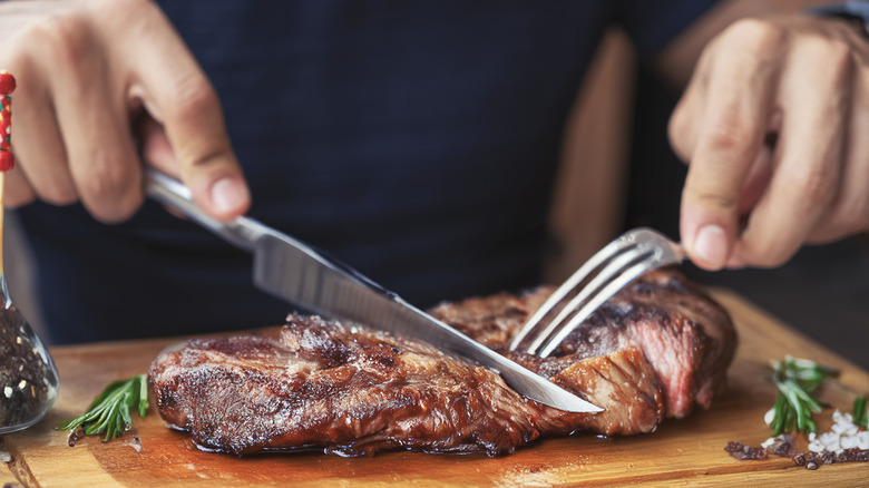 Hands cutting steak on wooden plate