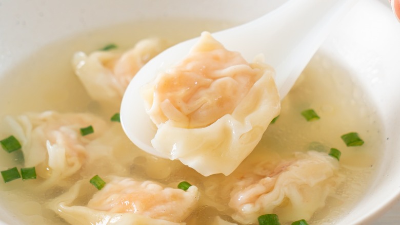 A boiled wonton dumpling in a spoon over wonton soup