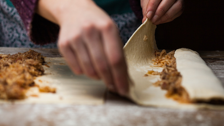 hands rolling phyllo dough around meat filling