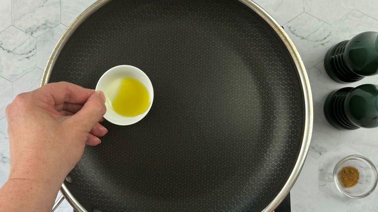 hand pouring oil into pan