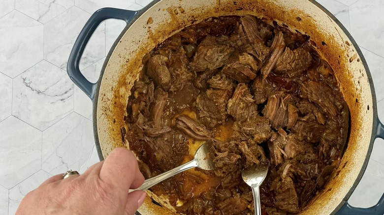 hands shredding meat with forks