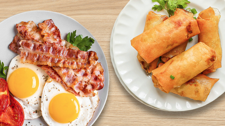 Plate of bacon and eggs next to plate of egg rolls